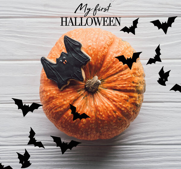 elevated view of pumpkin with homemade halloween cookie on wooden table with "my first halloween" lettering
