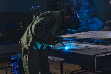 side view of welder in protection mask brazing metal at factory  clipart