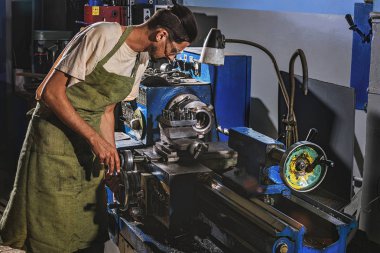 Erkek üretim işçisi koruyucu önlük ve gözlük fabrikasında makine aracını kullanarak yan görünüm
