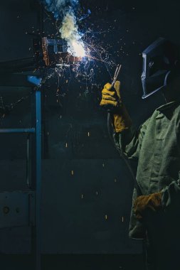 side view of manufacture worker welding metal with sparks at factory  clipart