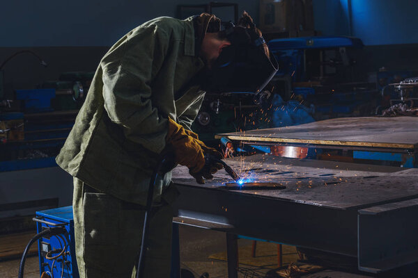 concentrated manufacture worker welding metal with sparks at factory 