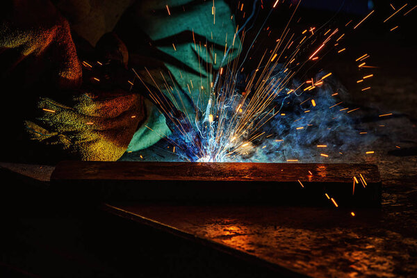cropped image of manufacture worker welding metal with sparks at factory 