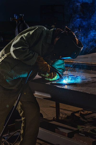 male manufacture worker welding metal with sparks at factory 