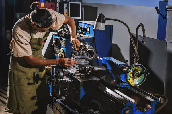 male manufacture worker in protective apron using machine tool at factory