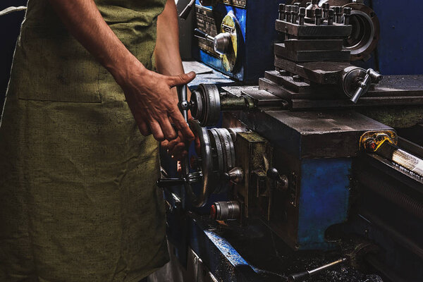 cropped image of male manufacture worker in protective apron using machine tool at factory