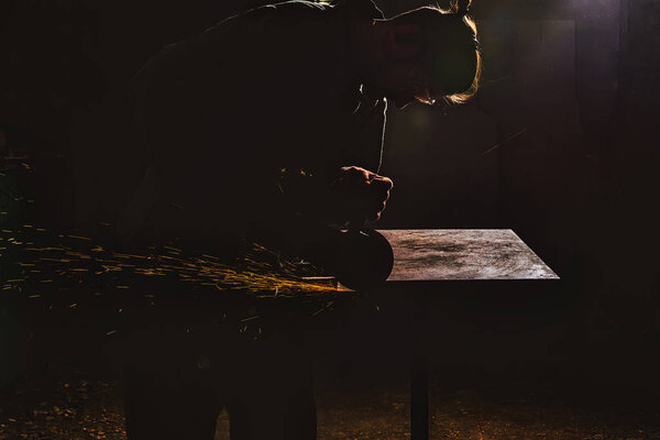 side view of manufacture worker in protective googles working with circular saw at factory