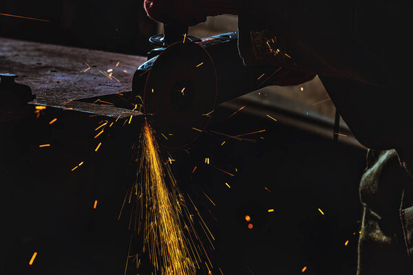 cropped image of manufacture worker using circular saw with sparkles at factory