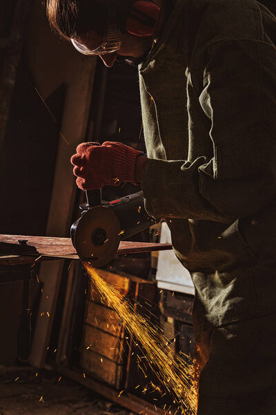 focused male worker in protective googles working with circular saw at factory