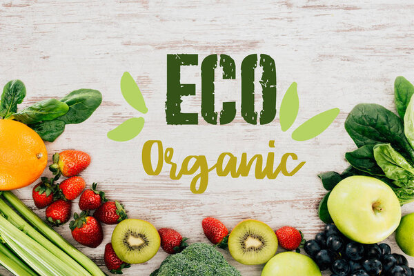 top view of arranged organic strawberries, vegetables and fruits on wooden tabletop with "eco organic" lettering