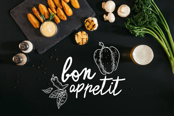 top view of delicious baked potatoes with sauce, spices and glass of beer on black with "bon appetit" lettering