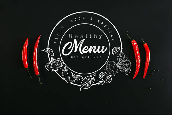 top view of red chili peppers and peppercorns on black background with "healthy menu" lettering in seal