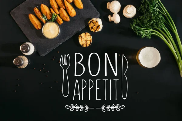 Top view of delicious baked potatoes with sauce, spices and glass of beer on black with "bon appetit" lettering with fork and knife — Stock Image Top View Delicious Baked Potatoes Sauce Spices Glass Beer Black Stock Image