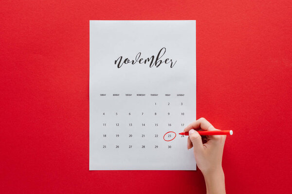 partial view of woman writing black friday in calendar for November isolated on red