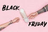 abgeschnittene Ansicht tätowierter Kunden, die Schnürsenkel von Turnschuhen isoliert auf rosa mit schwarzem Freitagsschild ziehen 