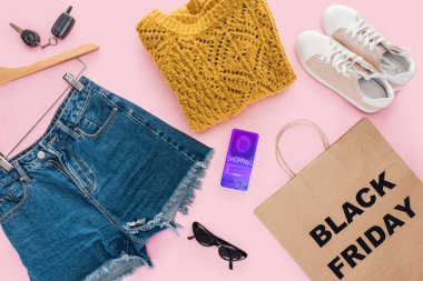 top view of trendy clothes, smartphone with shopping app and paper bag with black friday sign clipart