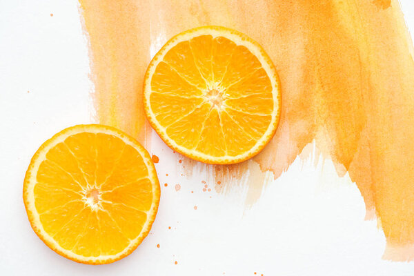 top view of two ripe orange pieces on white surface with orange watercolor