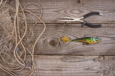 top view of fishing net, pair on nippers and fishing bait on wooden background clipart