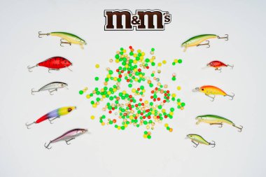 elevated view of colorful candies surrounded by fishing bait placed in rows and sign m&m's isolated on white  clipart