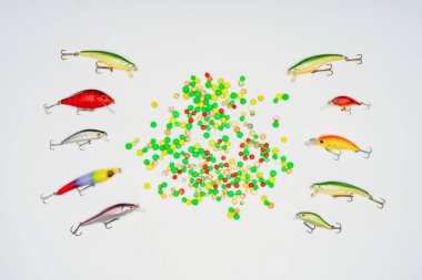 top view of colorful candies surrounded by fishing bait placed in rows isolated on white  clipart