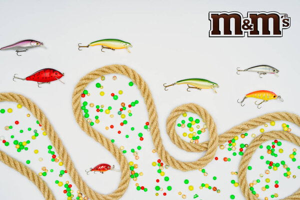 top view of fishing bait, colorful candies, nautical rope and sign m&m's isolated on white