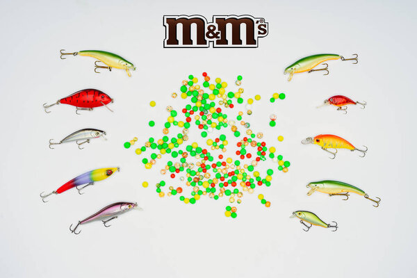 elevated view of colorful candies surrounded by fishing bait placed in rows and sign m&m's isolated on white 