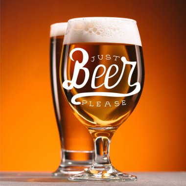 selective focus of arrangement of glasses of beer with froth on orange backdrop with 