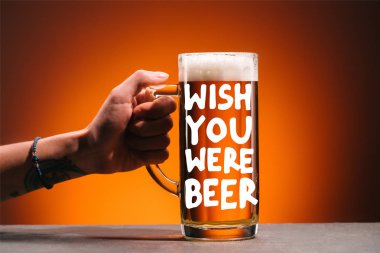 cropped shot of woman holding glass of cold beer with foam on orange backdrop with 