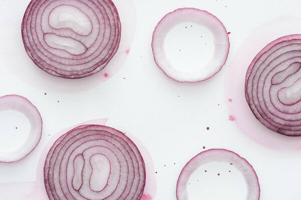 top view of slices of spicy red onion on white surface with pink watercolor blots