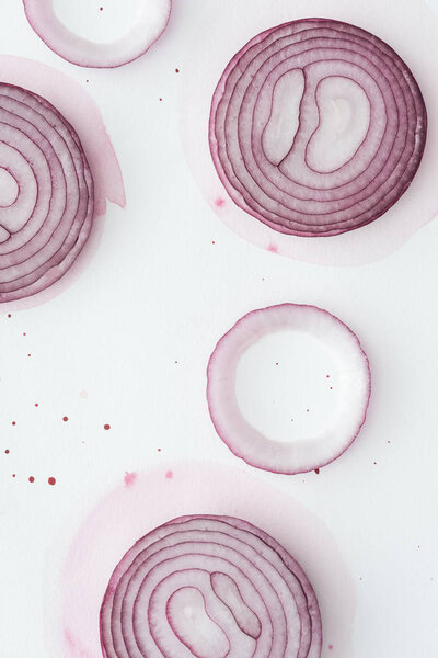 top view of raw slices of red onion on white surface with pink watercolor blots