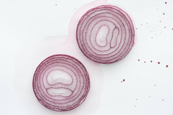 top view of two slices of red onion on white surface with pink watercolor blots