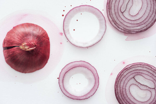 top view of red onion with slices and rings on white surface with pink watercolor blots