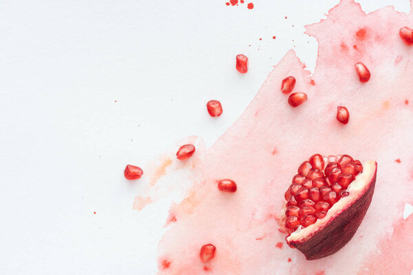 top view of pomegranate seeds on white surface with red watercolor strokes