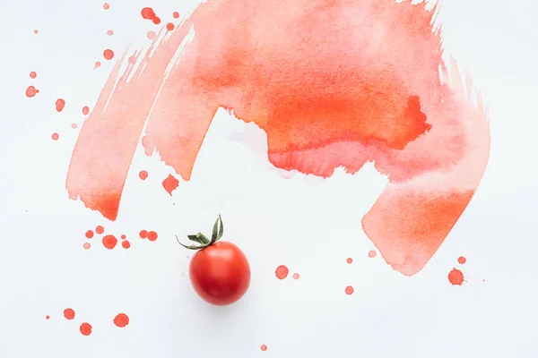 top view of single cherry tomato on white surface with red watercolor strokes