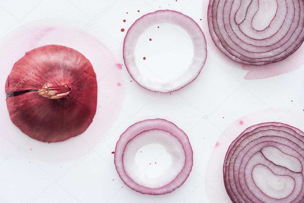 top view of red onion with slices and rings on white surface with pink watercolor blots
