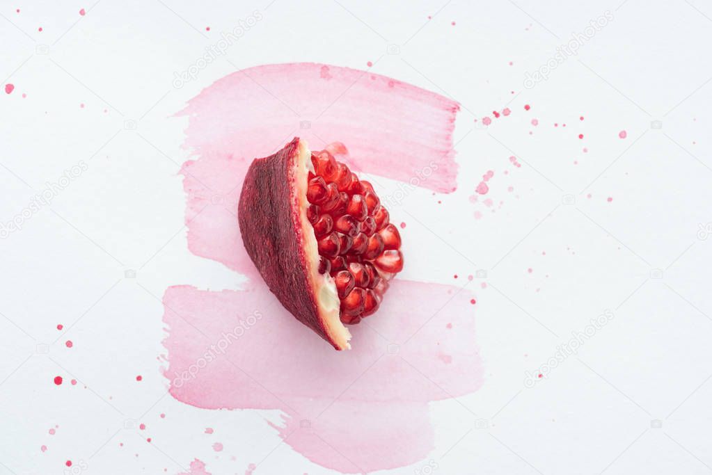 top view of piece of pomegranate on white surface with pink watercolor strokes