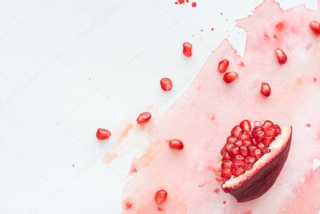 top view of pomegranate seeds on white surface with red watercolor strokes