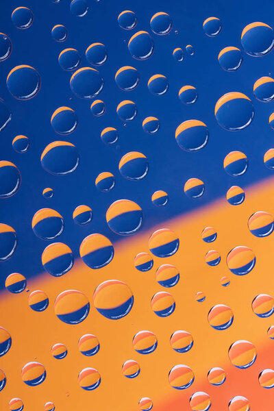 close-up view of transparent water drops on blue and orange abstract background