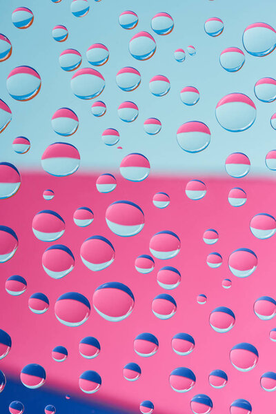 close-up view of transparent droplets on pink and blue abstract background 