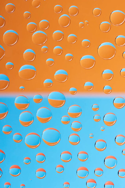 close-up view of transparent water drops on blue and orange background