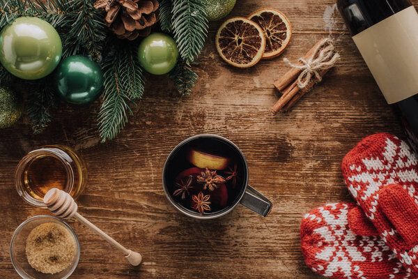 elevated view of cup of mulled wine and winter mittens on wooden table, christmas concept