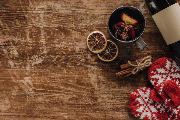 top view of mulled wine in cup, mittens and wine bottle on wooden table, christmas concept