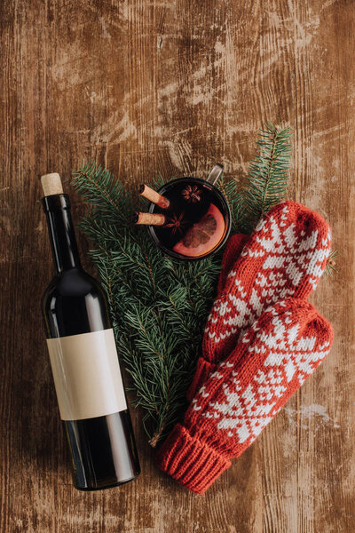 вид сверху на бутылку вина, чашку глинтвейна, рождественские елочные ветки и варежки на деревянном столе
