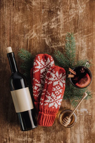 top view of wine bottle, cup of mulled wine and winter mittens on wooden tabletop, christmas concept