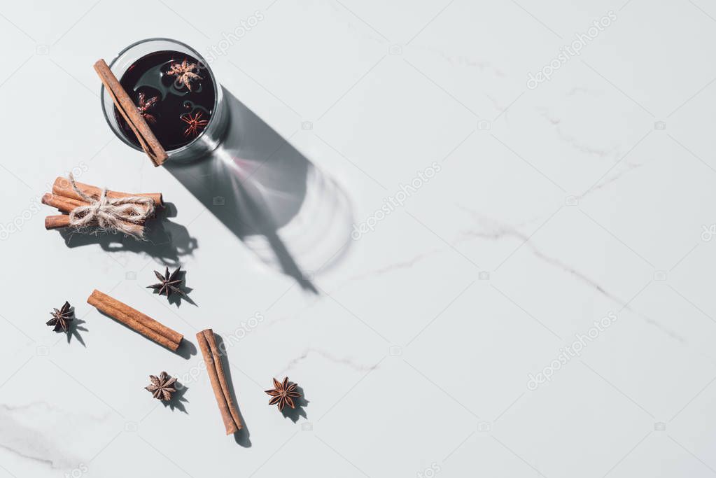 elevated view of mulled wine in glass and scattered cinnamon sticks on white tabletop