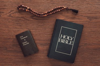 top view of holy bible with new testament and beads on wooden table clipart