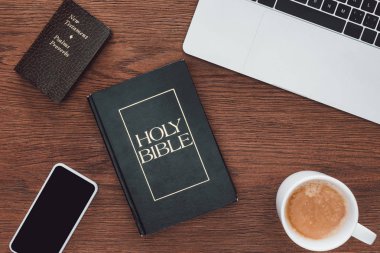 top view of holy bible with new testament, gadgets and coffee on wooden table clipart