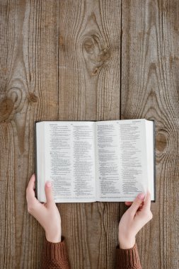 cropped shot of woman holding opened holy bible on wooden tabletop clipart
