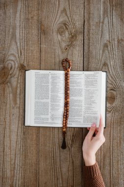 cropped shot of woman with holy bible and beads on wooden tabletop clipart