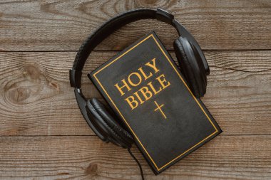 top view of holy bible with headphones on wooden tabletop clipart