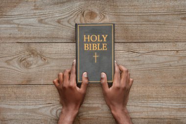 cropped shot of man holding holy bible on rustic wooden table clipart